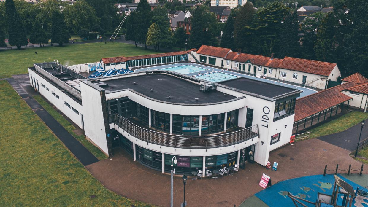 Adeilad lido gwyn, gyda'r pwll nofio yn y golwg ym Mharc Ynysangharad, Pontypridd