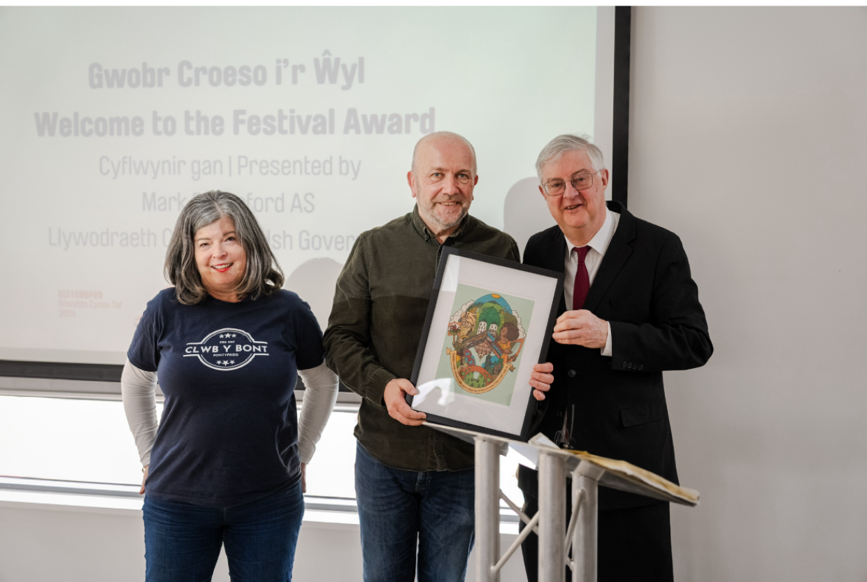 Mark Drakeford yn cyflwyno gwobr croeso i'r wyl i Glwb y Bont