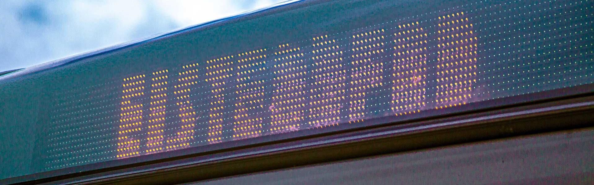 A digital display on a bus showing the destination 'EISTEDDFOD' against a background of a partly cloudy sky